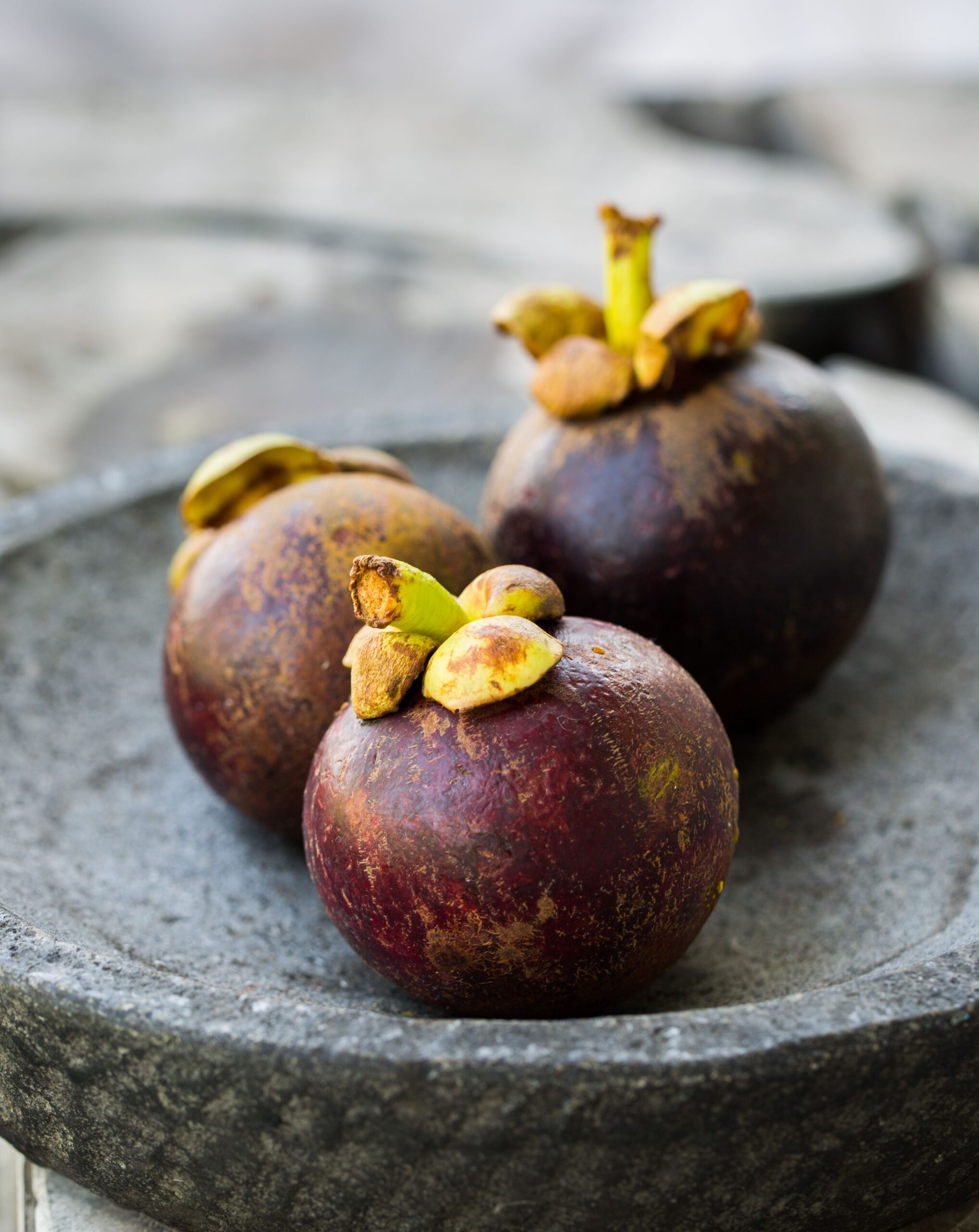 Close-up photo of ripe mangosteen fruits placed on a rustic stone plate, showcasing fresh tropical flavor.